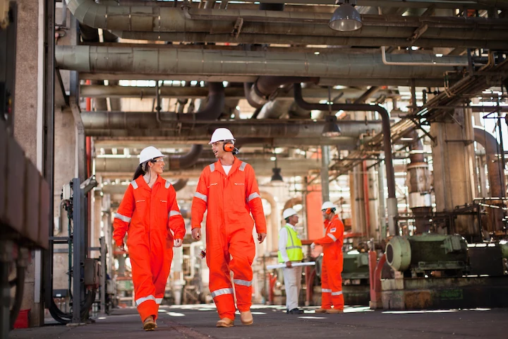 Workers in protective gear walking through an oil processing plant