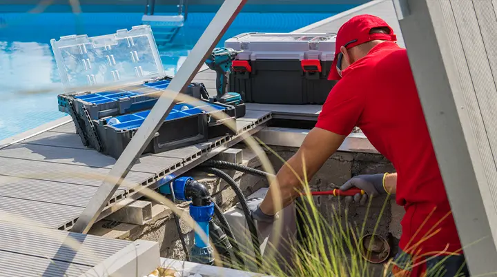 Technician servicing pool equipment beside a swimming pool